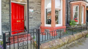 A townhouse with a red door, stone facade, and a small garden with purple flowers. - Sefton House (Keswick)