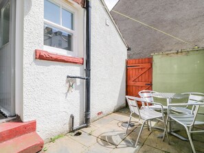A small outdoor patio with a white wall, a window, a red door, and a green garage door. - Sefton House (Keswick)