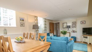 Een moderne woonkamer met een houten eettafel, een blauwe bank en een flatscreen televisie.