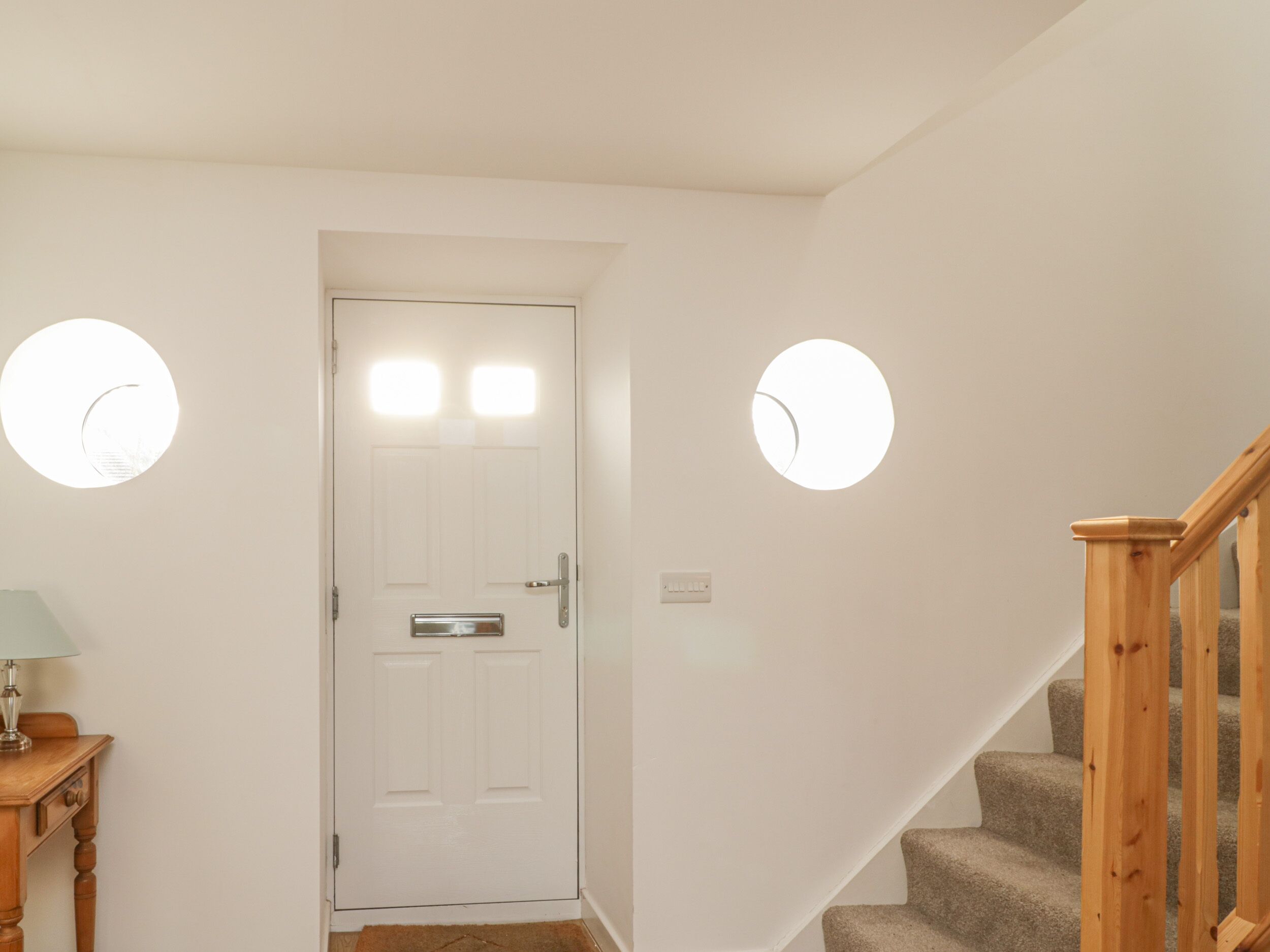 A hallway with a white door, a wooden table with a lamp, and a staircase with wooden railings.