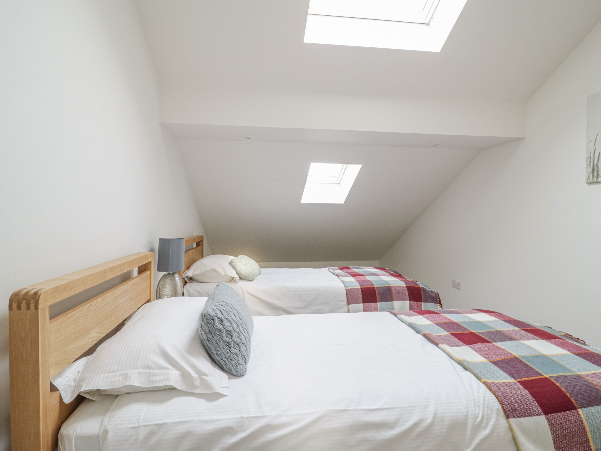 A bedroom with two beds, a skylight, and a wooden headboard.
