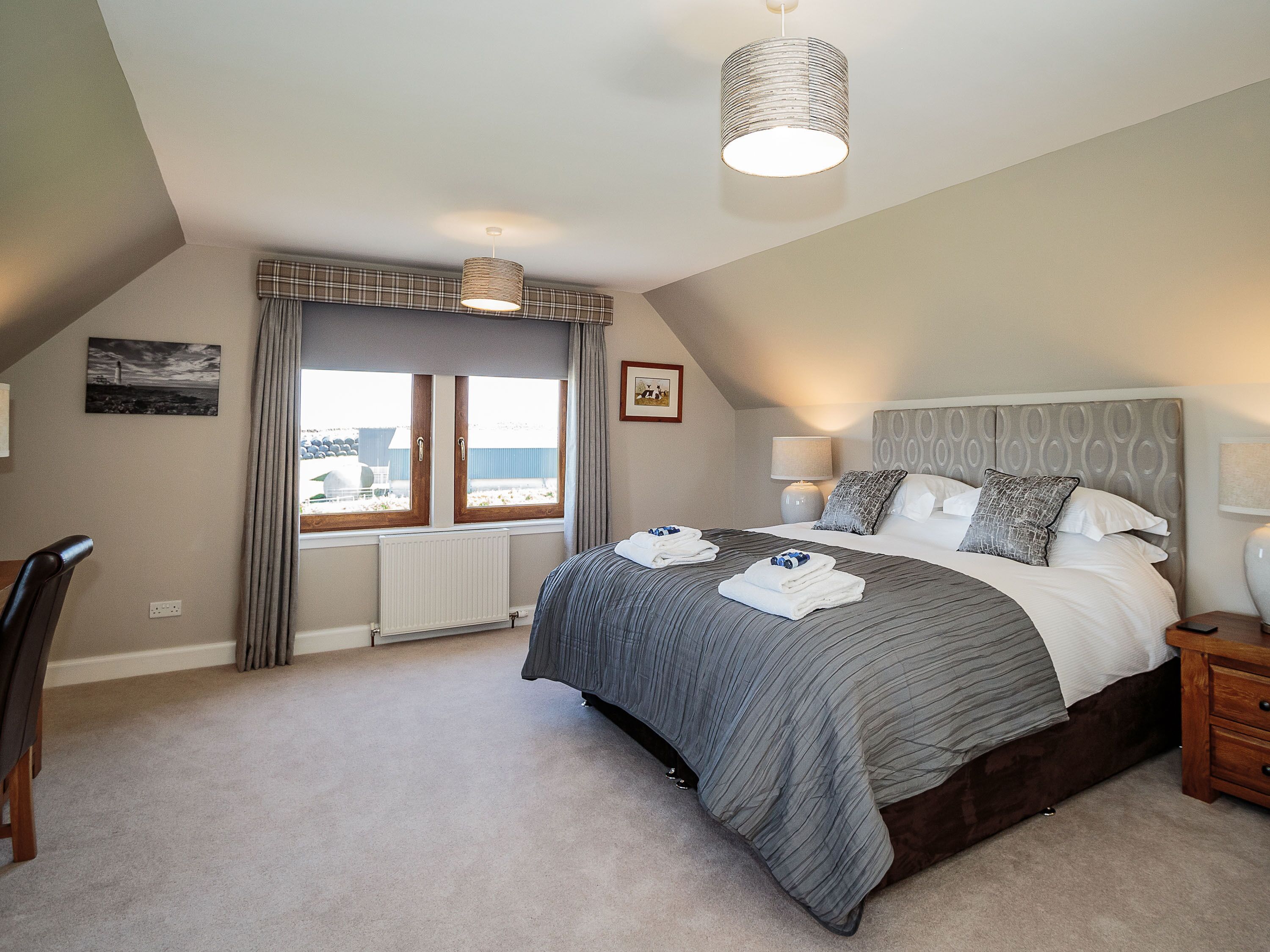 A bedroom with a large bed, a bedside table, a lamp, a radiator, and a window with curtains.