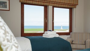 Ein Hotelzimmer mit zwei Betten, Meerblick und einem Leuchtturm in der Ferne.