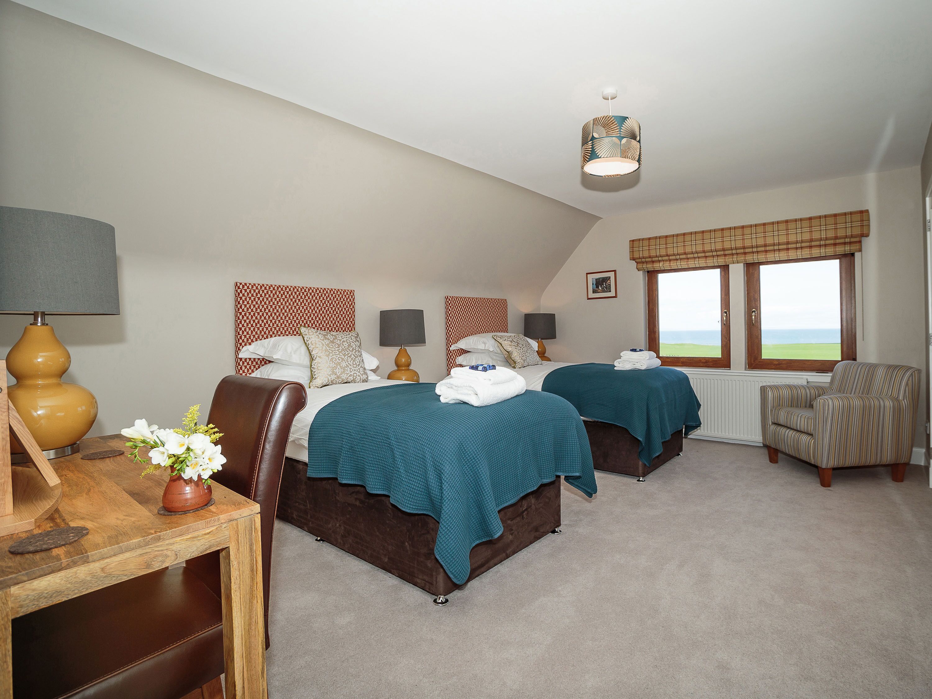 A hotel room with two beds, a desk with a lamp, a chair, and a window with a view.