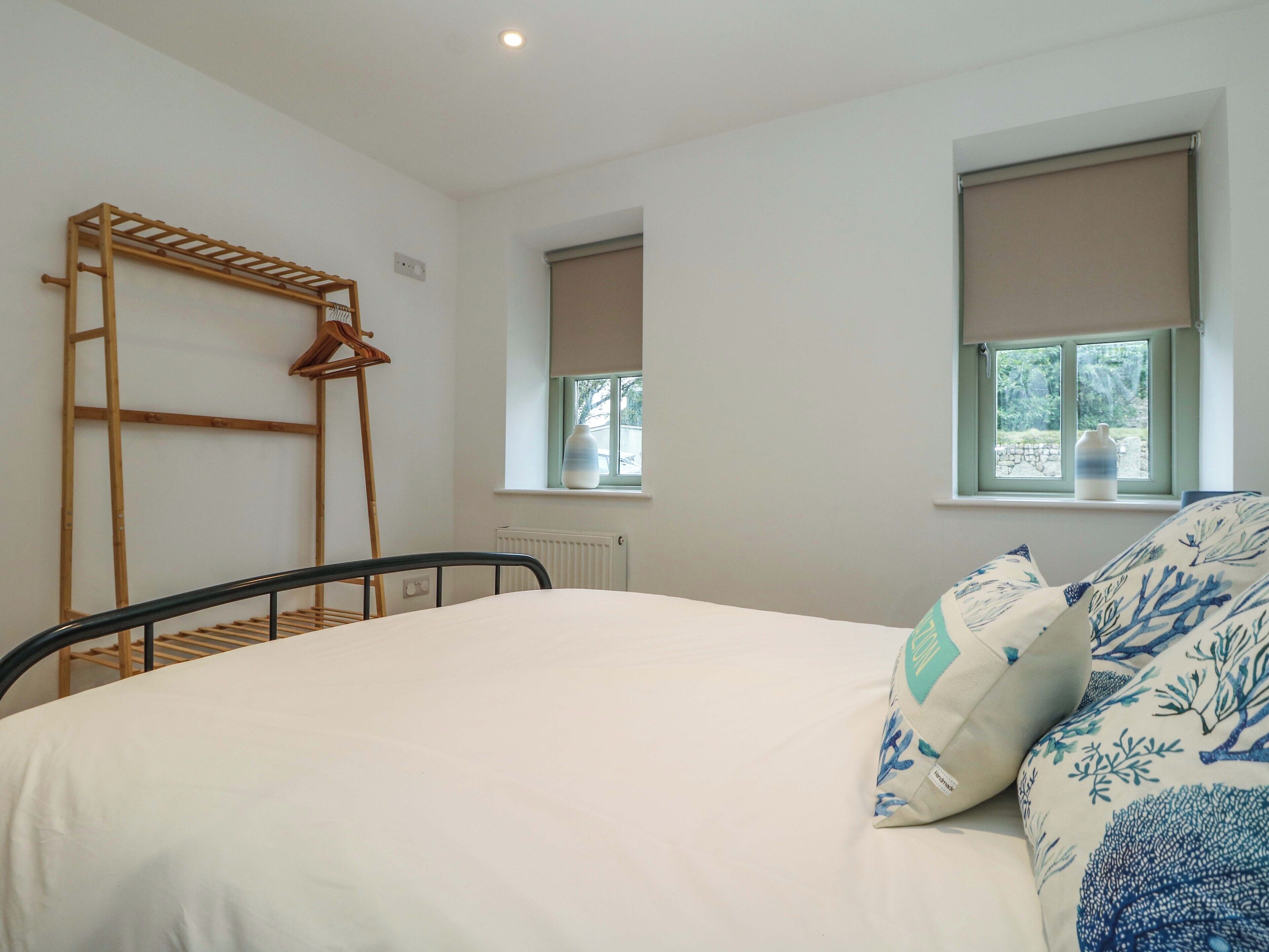 Un dormitorio con cama, un tendedero de madera, dos ventanas con persianas y un radiador.