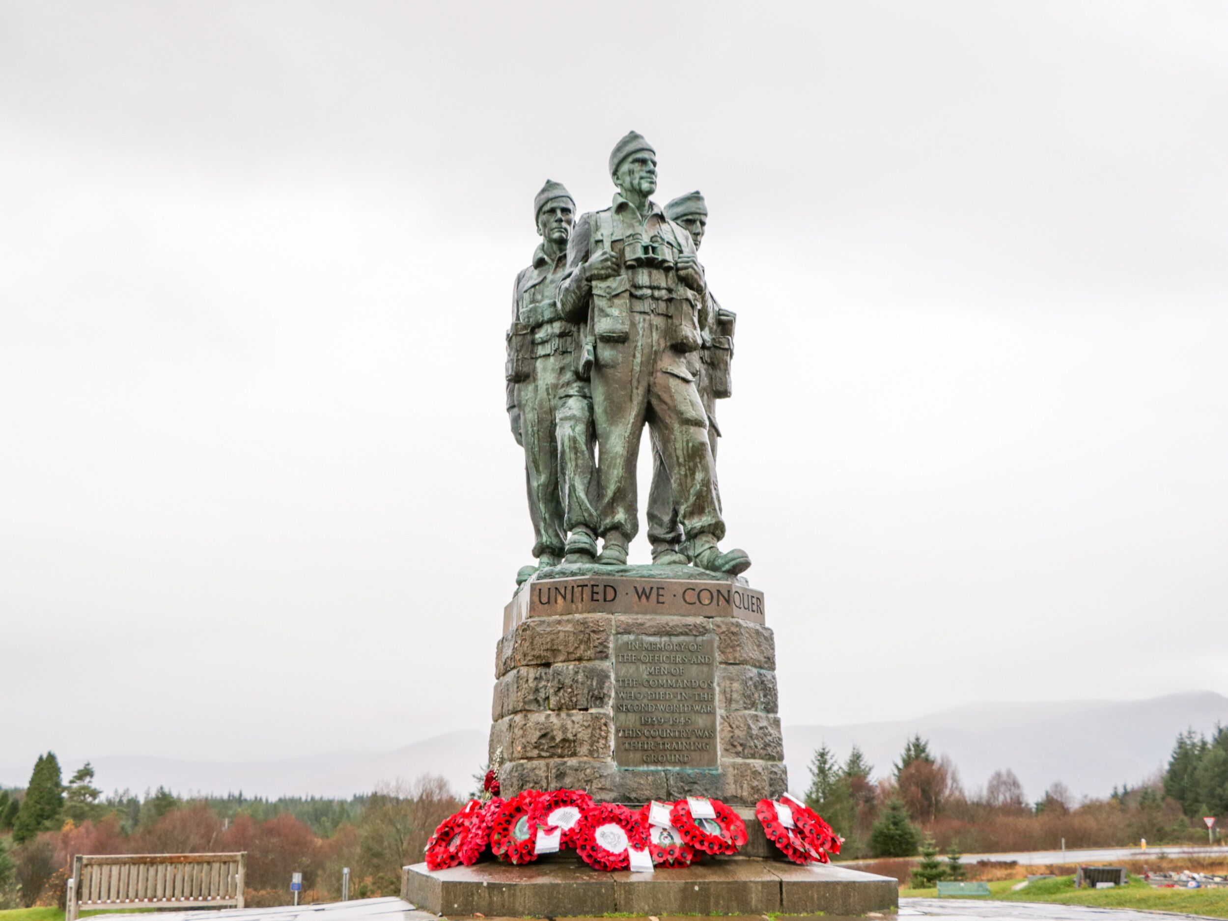 A memorial statue with inscriptions, surrounded by red poppy wreaths.