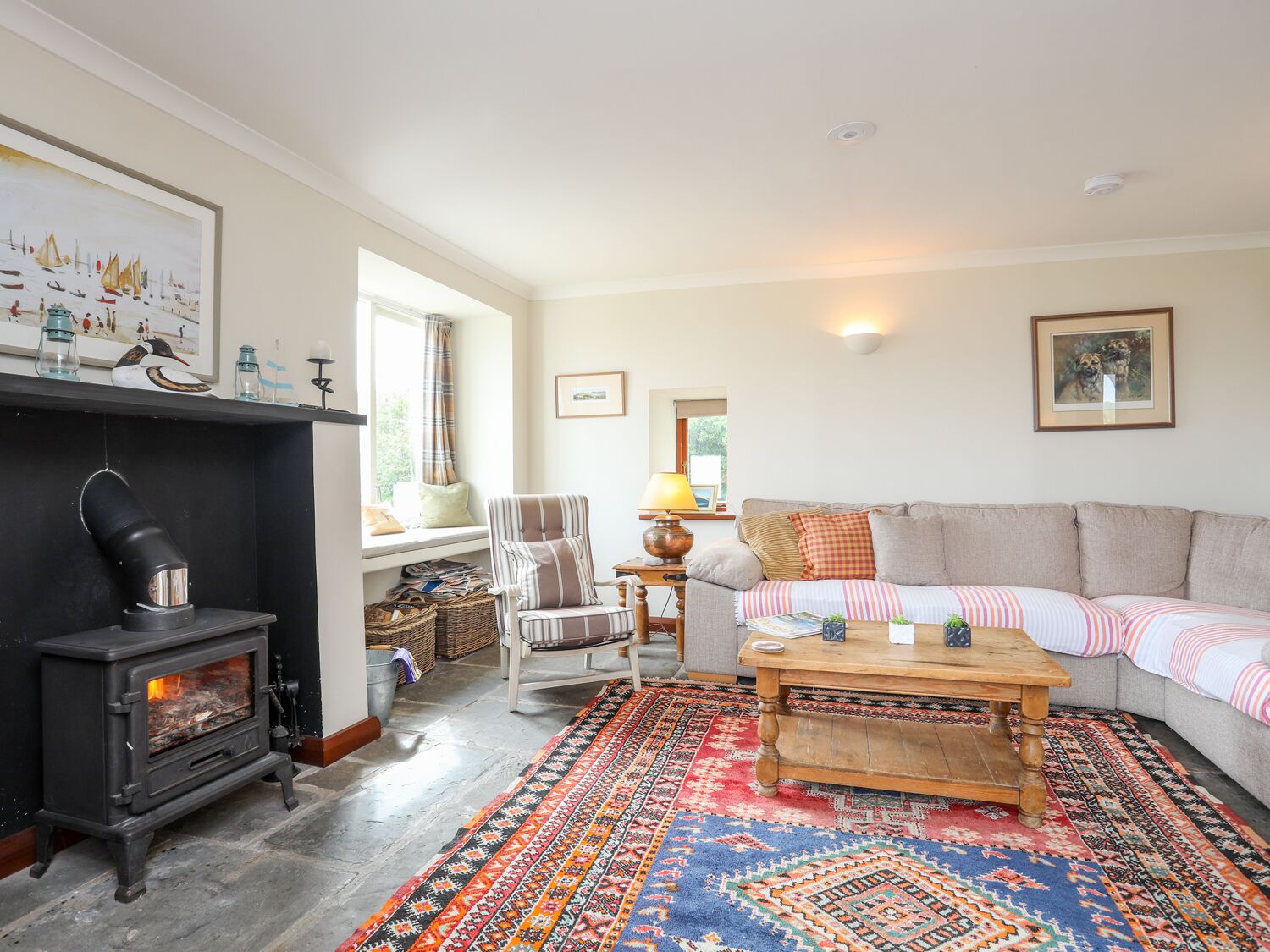 A cozy living room with a fireplace, a sofa, a striped armchair, a wooden coffee table, and a colorful rug.