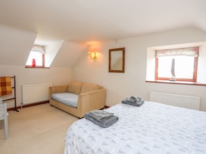 Ein Schlafzimmer mit einem Bett, einer Couch, einem Heizkörper, einem Fenster mit Vorhängen, einem wandmontierten Spiegel und einem kleinen Tisch mit Handtüchern.