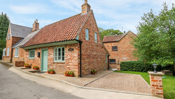 A traditional brick house with a tiled roof, a front door, and a small porch area with potted plants. - Lizzies Cottage (Horncastle)