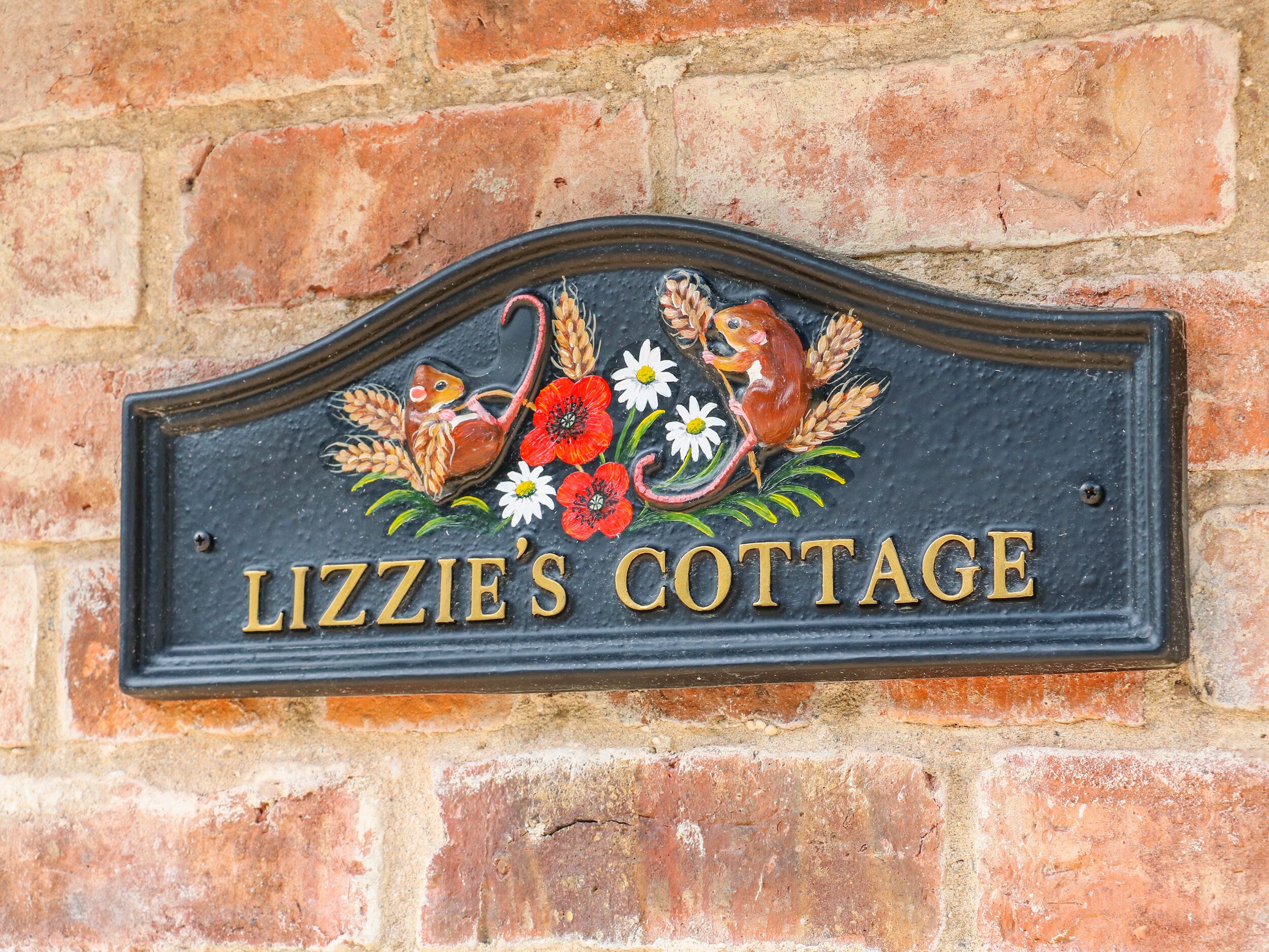 A sign for Lizzie's Cottage with a decorative emblem featuring birds and flowers.