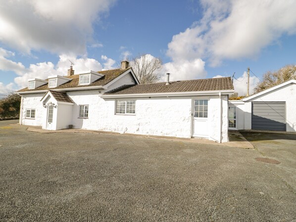 A two-story white house with a garage, a driveway, and a clear sky. - Rhous (Tyn-y-Gongl)