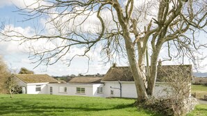 A white building with a tiled roof, surrounded by a grassy area and a large tree.