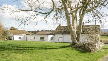 A white building with a tiled roof, surrounded by a grassy area and a large tree.
