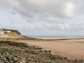 A beach with rocky terrain and a building on the left. - Rhous (Tyn-y-Gongl)