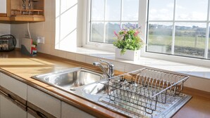 A kitchen with wooden cabinets, a stainless steel sink, and a window with a view of the countryside.