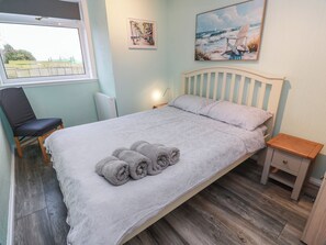 A neatly made bed with rolled towels, a chair, a bedside table, and artwork on the walls. - Mardan (Dumfries)