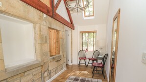 A room with stone walls, wooden beams, a plaid rug, and a dining area with chairs and a table. - Nursery Cottage (Morpeth)