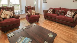A living room with a wooden coffee table, two armchairs, and a sofa, all in a deep red color. - Nursery Cottage (Morpeth)