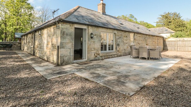 A stone cottage with a tiled patio, a chimney, and a door leading to a room. - Nursery Cottage (Morpeth)