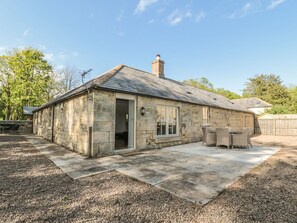 Une petite maison en pierre avec une terrasse carrelée, une cheminée et une porte donnant sur une pièce.