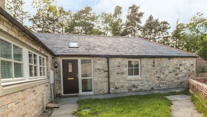 A stone building with a dark roof, a front door, and a small window. - Nursery Cottage (Morpeth)