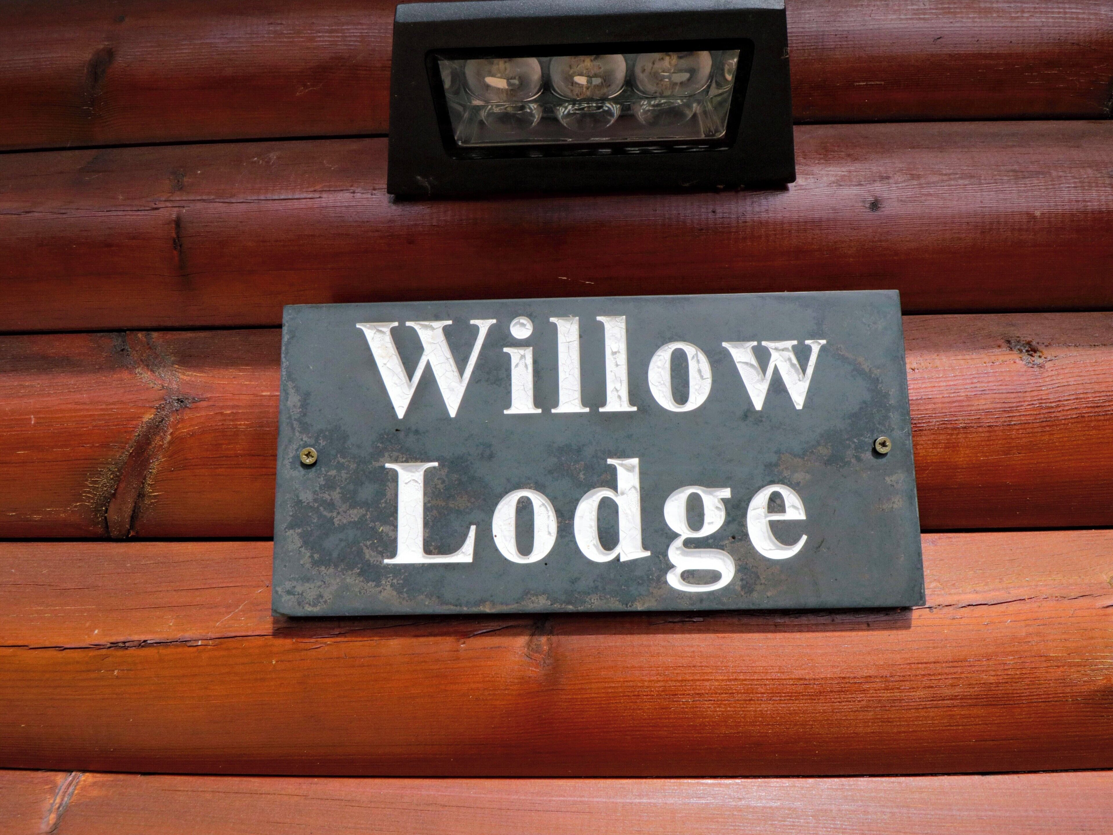 A sign with the text "Willow Lodge" mounted on a wooden wall.