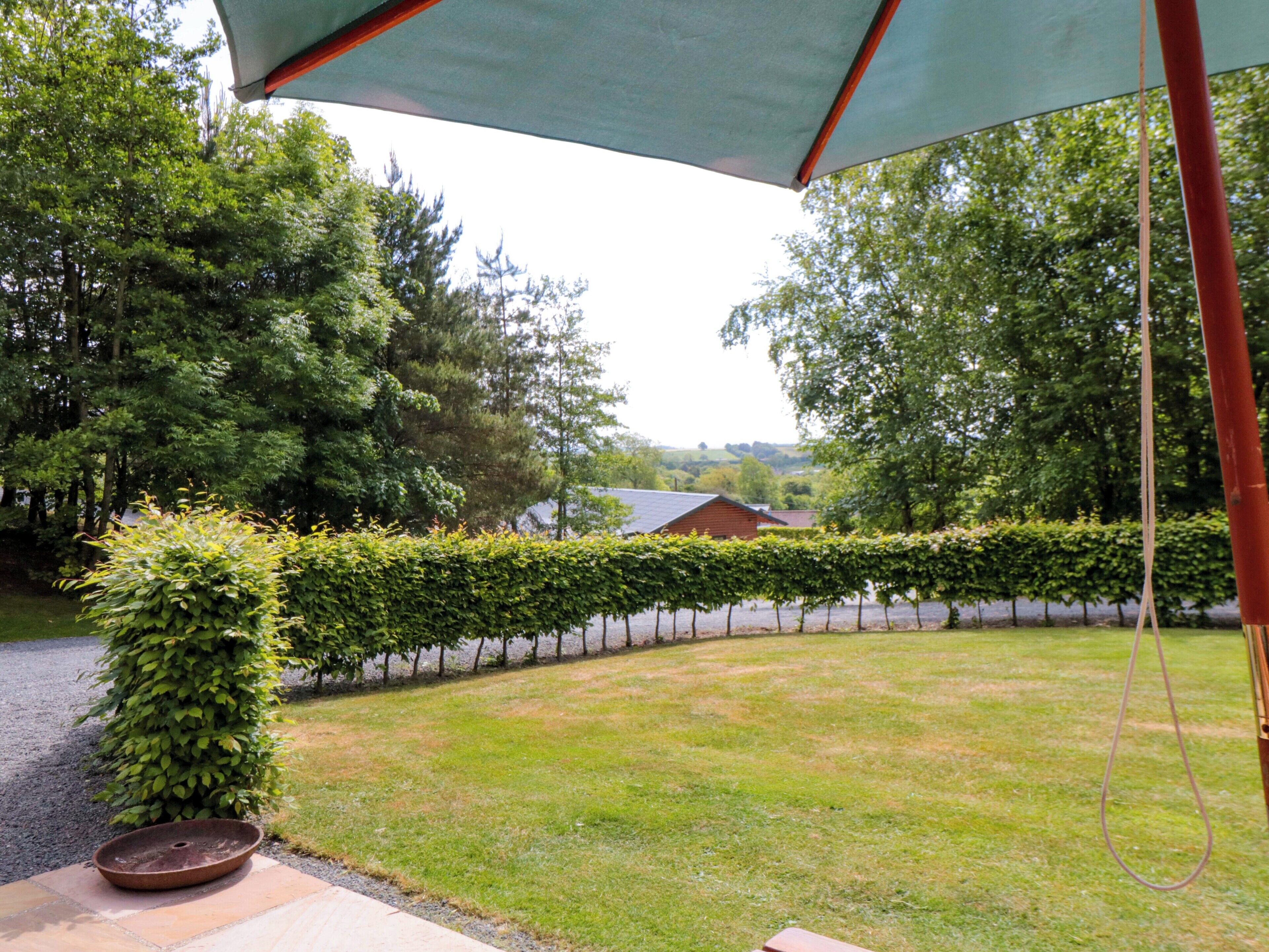 Un jardin bien entretenu, avec une haie taillée avec soin, un chemin de gravier et un bâtiment rustique en arrière-plan.
