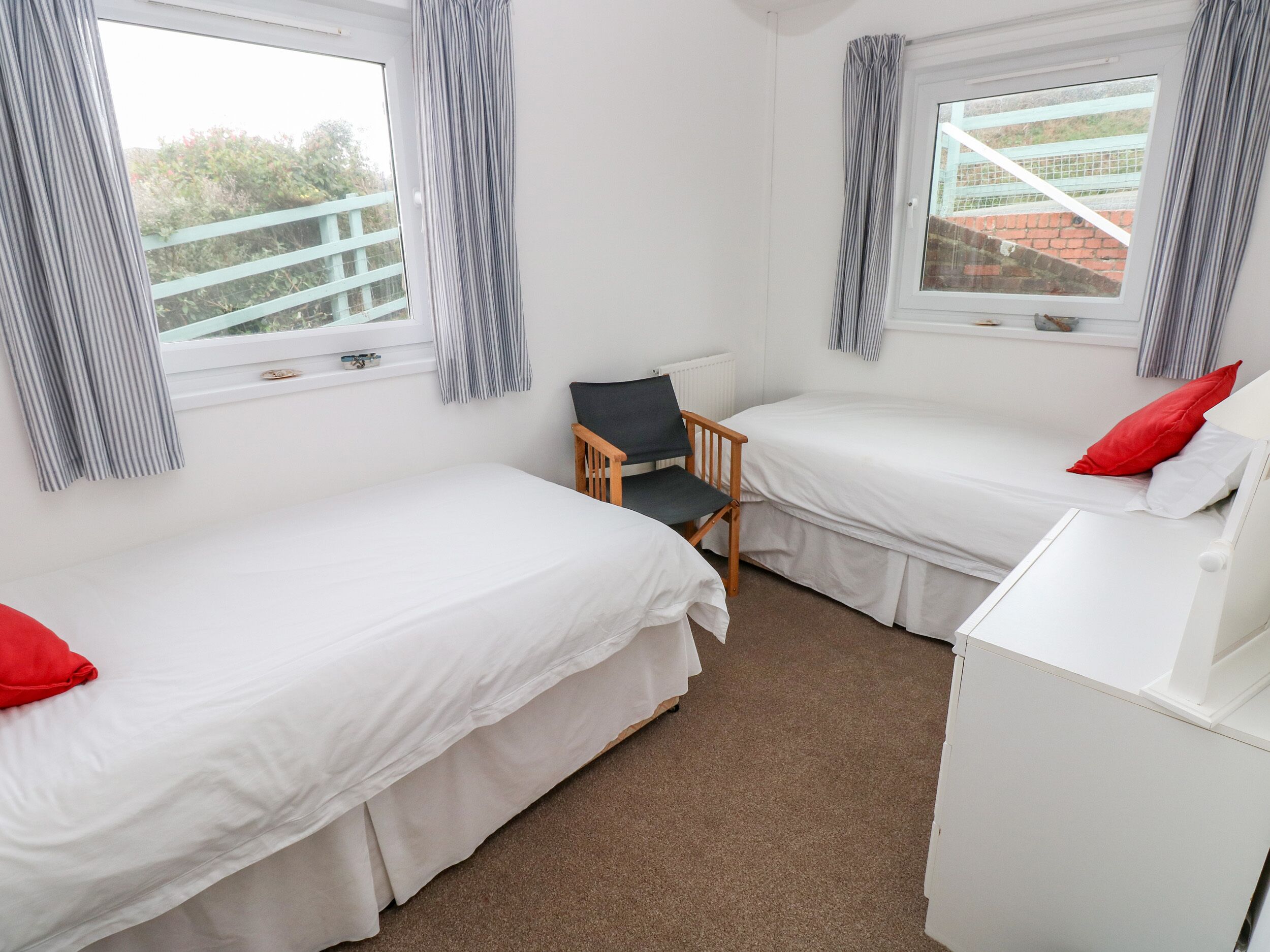 A room with two single beds, a wooden chair, a white dresser, and a window with curtains.