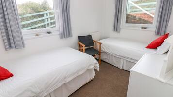 A room with two single beds, a wooden chair, a white dresser, and a window with curtains.