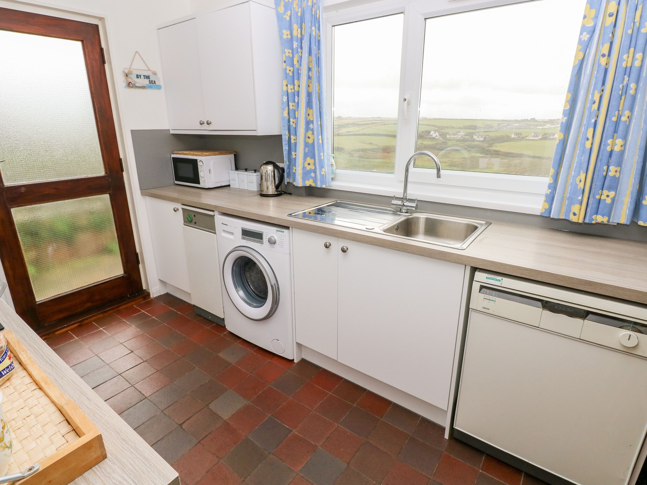 A compact kitchen with a washing machine, a microwave, a kettle, and a sink.