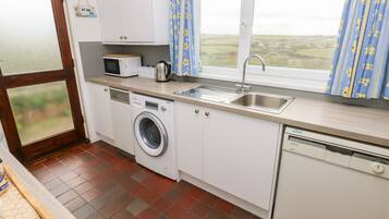 A compact kitchen with a washing machine, a microwave, a kettle, and a sink.