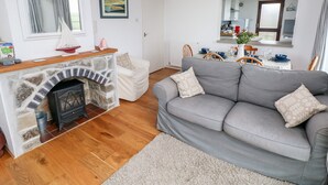 Ein gemütliches Wohnzimmer mit Kamin aus Naturstein, einem grauen Sofa und einem Essbereich mit Tisch für vier Personen.