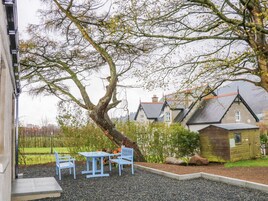 Un patio con una mesa, sillas, un árbol y un edificio de techo inclinado al fondo.