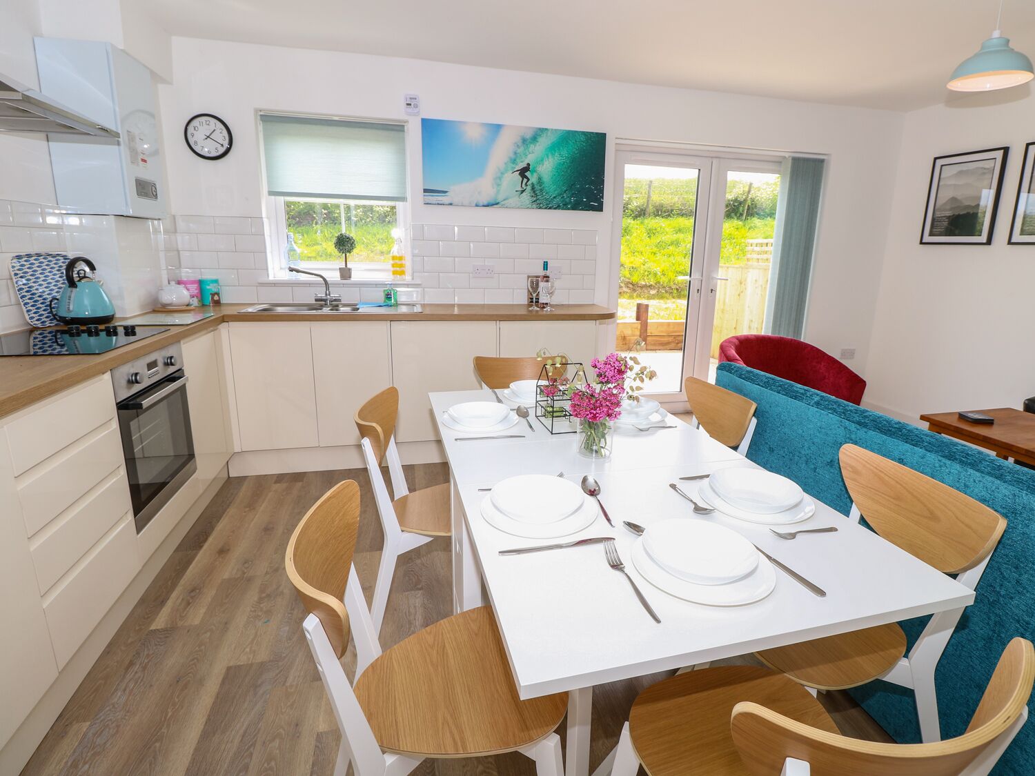 A modern kitchen with white cabinets, a built-in oven, and a window overlooking a garden.
