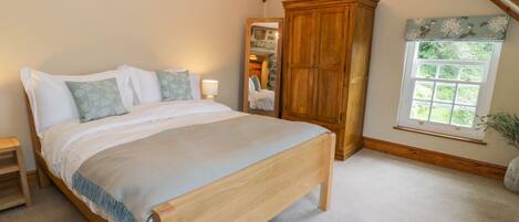 A bedroom with a large bed, wooden wardrobe, and a window with a view of greenery.