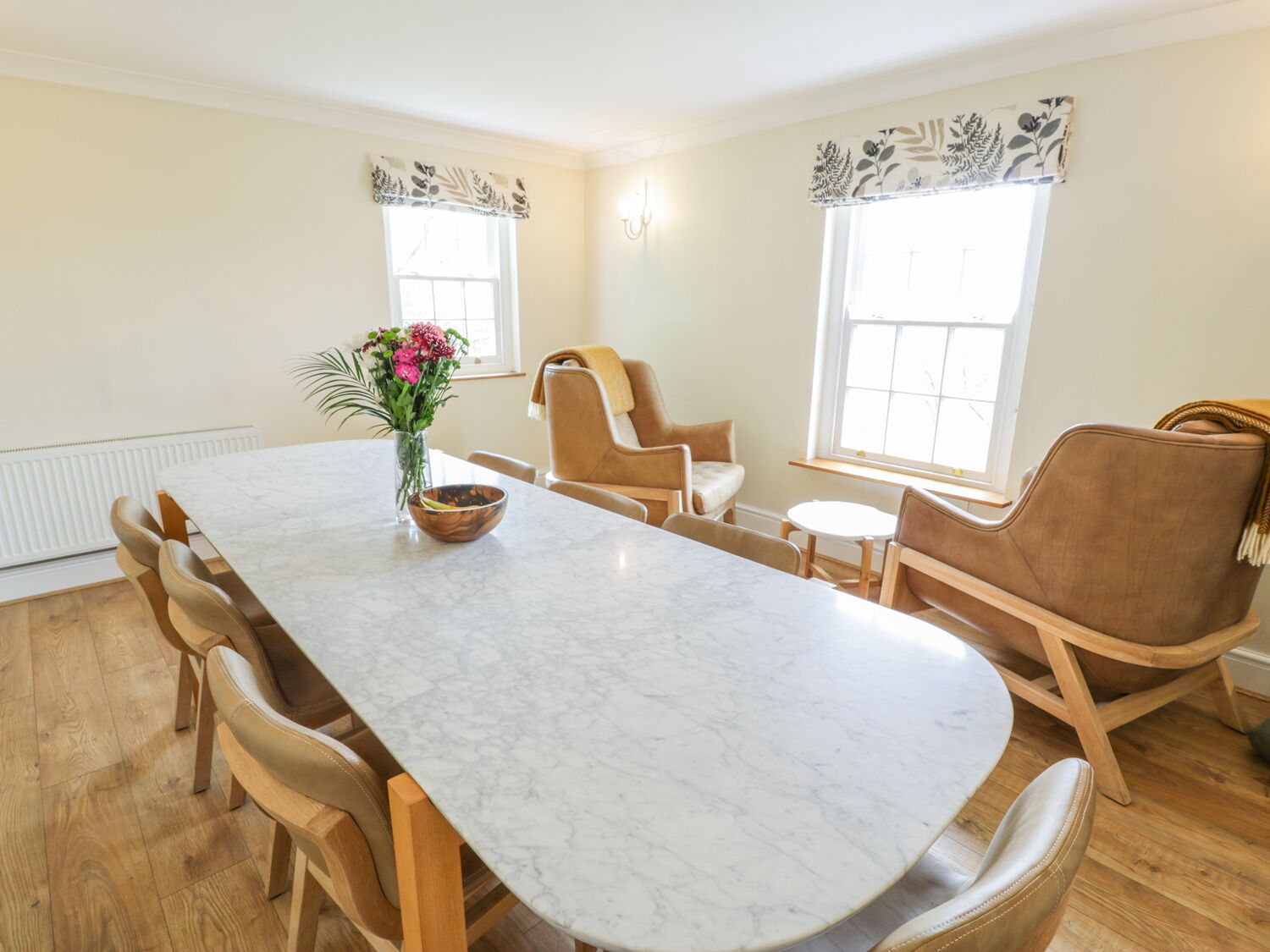 A dining area with a marble table, wooden chairs, and a vase of flowers.