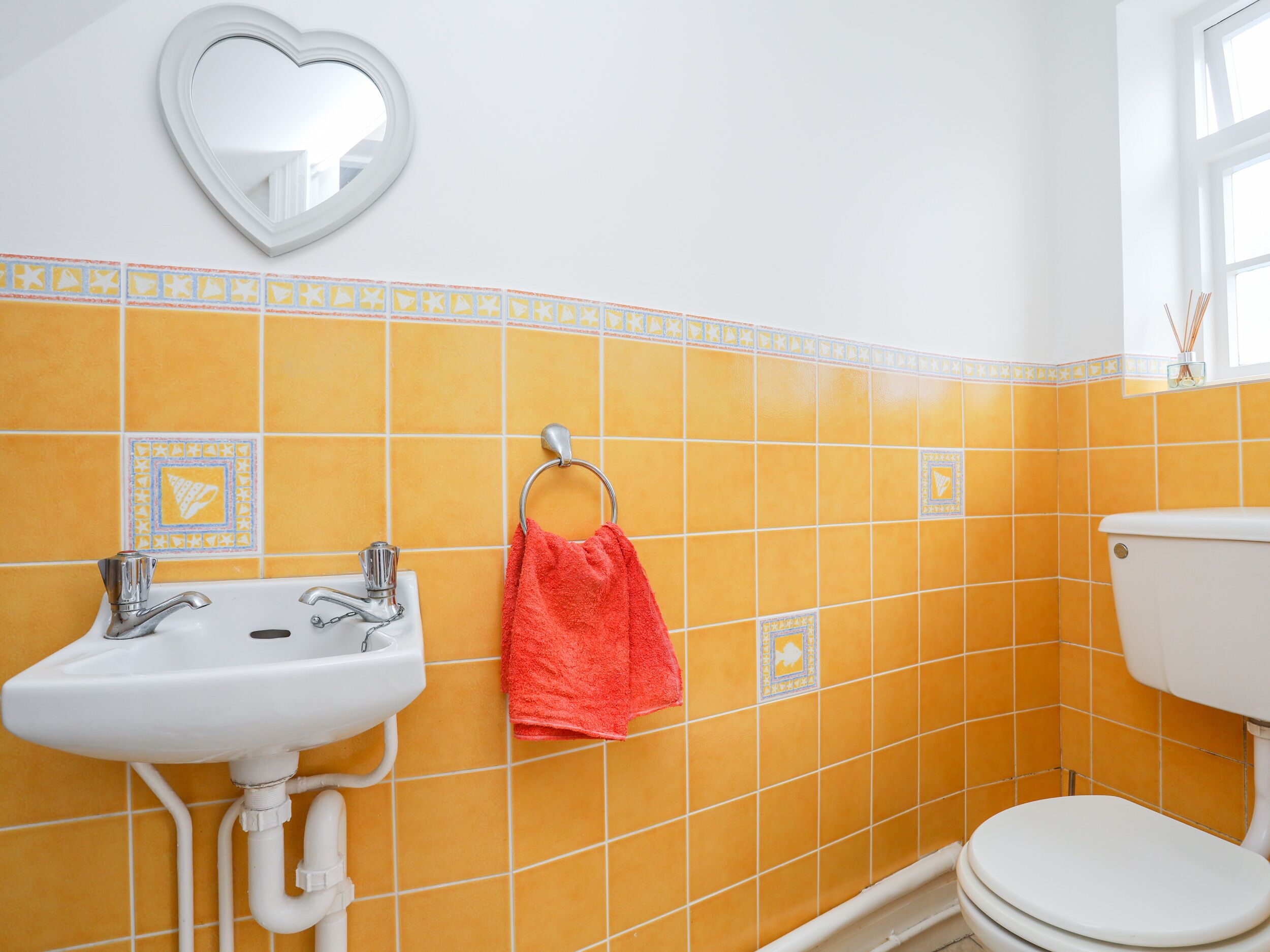 A bathroom with yellow tiles, a white sink, a red towel, and a toilet.