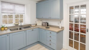 A modern kitchen with light blue cabinets, a stainless steel sink, and a window with a view of the outdoors. - The Pink House (Rhosneigr)