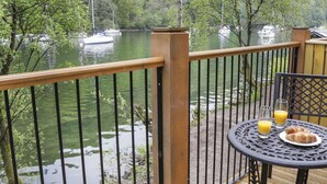 A balcony with a view of a river, a table with a plate of food and glasses of orange juice, and a wooden railing. - Gilson (Ambleside)