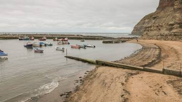Enjoy the serene coastal scenery and scenic views from the cliff overlooking the sandy beach and moored boats.