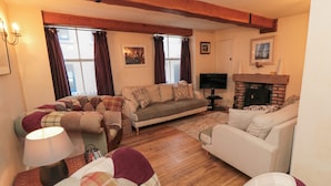 A cozy living room with a fireplace, two sofas, a television, and a window with curtains. - Salmon Cottage (Saltburn-by-the-Sea)