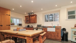 A kitchen with wooden cabinets, a central island, and a window overlooking the street. - Salmon Cottage (Saltburn-by-the-Sea)