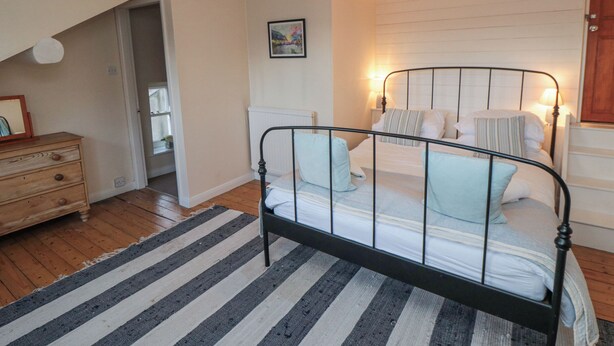 A bedroom with a bed, a dresser, a window, and a hanging light fixture. - Salmon Cottage (Saltburn-by-the-Sea)