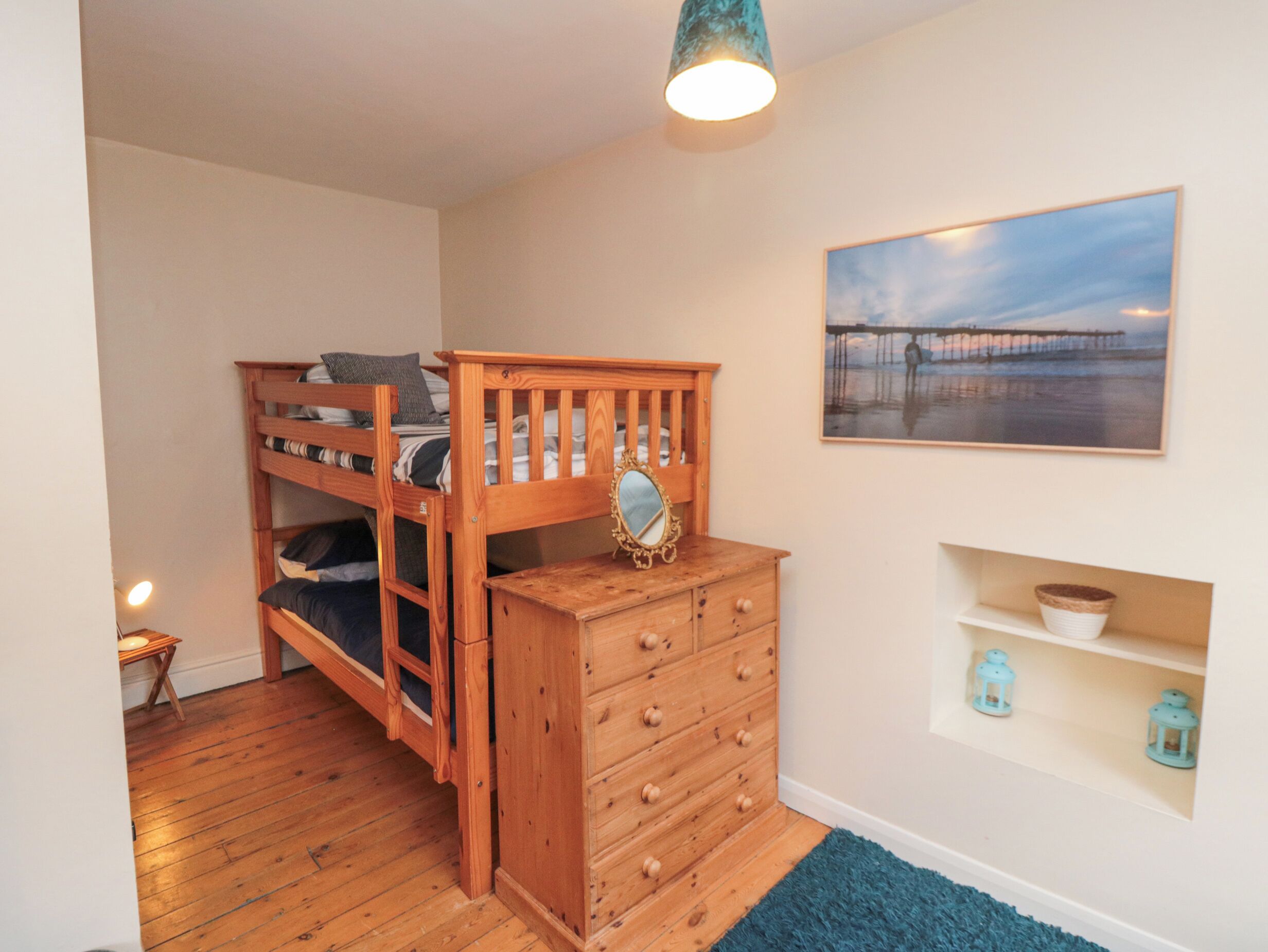 Une chambre à coucher avec un lit superposé, une commode, un miroir, un tableau et une étagère ornée d’objets décoratifs.