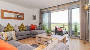 A modern living room with a grey sectional sofa, a wooden coffee table, and a balcony with a view of the countryside. - 8 Cribbar (Newquay)