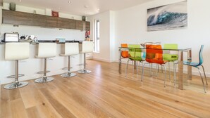 A modern kitchen with wooden cabinets, a bar area with four stools, and a dining table with colorful chairs. - 8 Cribbar (Newquay)