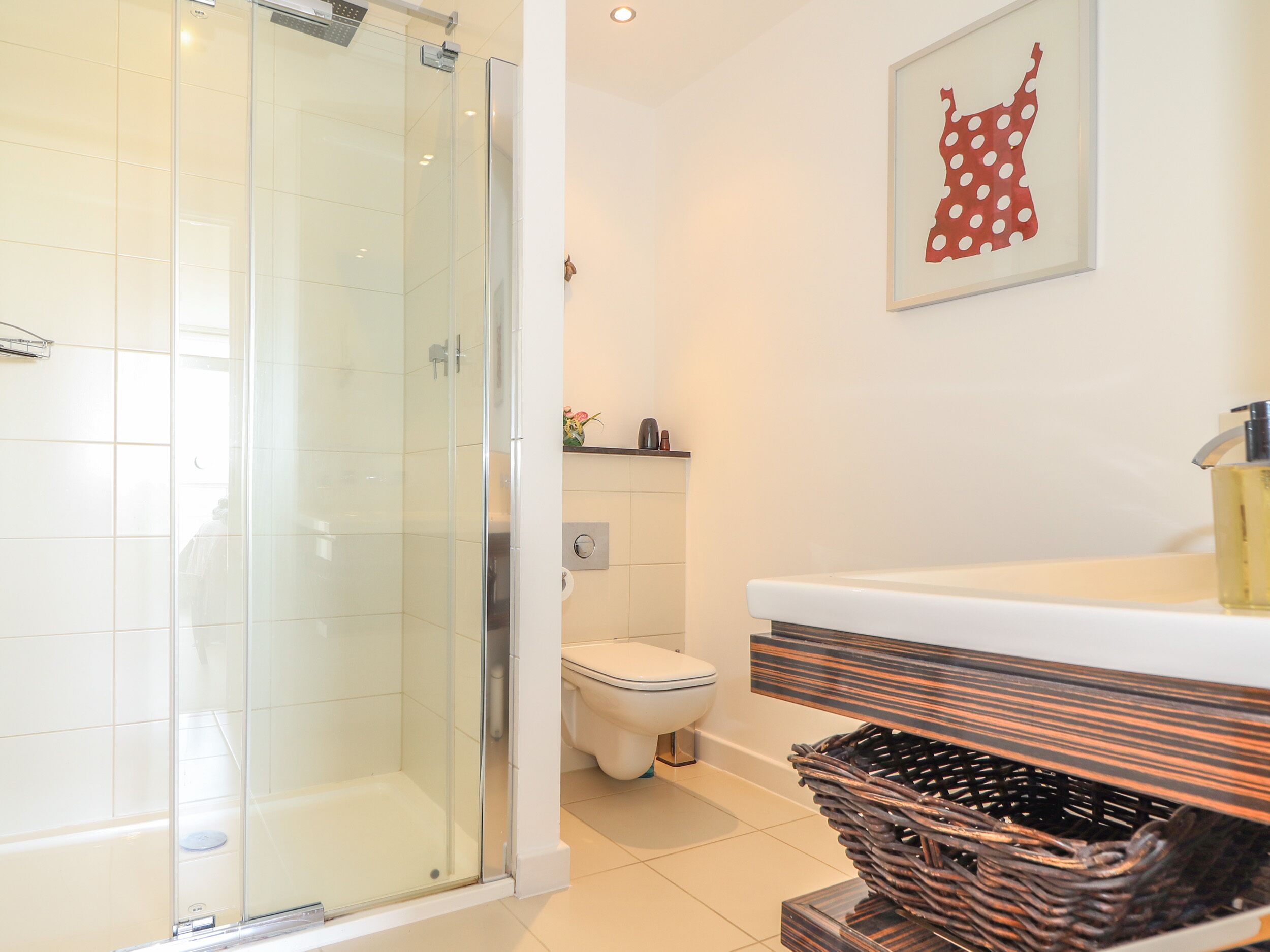 A modern bathroom with a glass-enclosed shower, a white toilet, and a wooden vanity with a basket of toiletries.