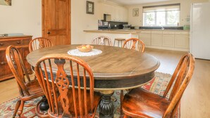 Une salle à manger avec une table et des chaises en bois, une cuisine à l’arrière-plan et un tapis à motifs sur le sol.