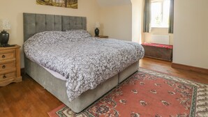 Une chambre à coucher avec un grand lit, une table de chevet, une lampe, un tableau au mur, une fenêtre avec des rideaux et un radiateur.