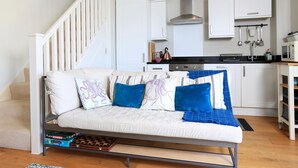 A modern living room with a sofa, a staircase, and a kitchen area with white cabinets and a black countertop. - The Reach (Kingsbridge)